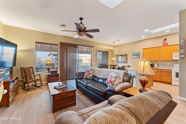 living room with ceiling fan, light hardwood / wood-style floors, and a skylight