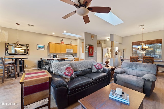 living room with a skylight, ceiling fan with notable chandelier, and light wood-type flooring