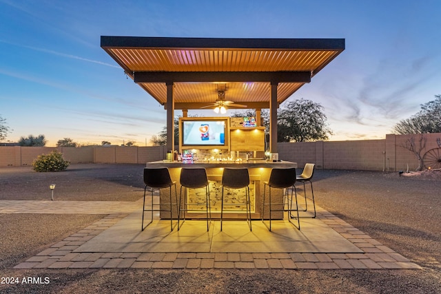 patio terrace at dusk featuring ceiling fan and a bar