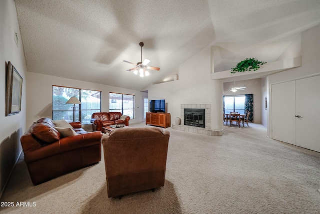 living area featuring a tiled fireplace, a ceiling fan, carpet, and a textured ceiling