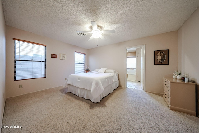 bedroom with visible vents, ensuite bathroom, a ceiling fan, a textured ceiling, and light colored carpet