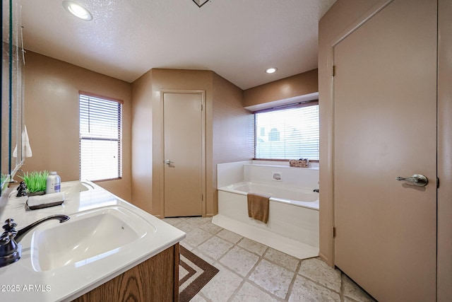 full bathroom with double vanity, recessed lighting, a sink, a textured ceiling, and a garden tub