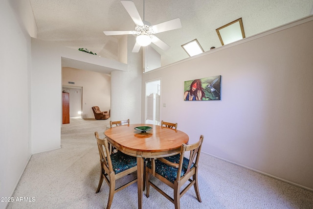 dining space featuring baseboards, ceiling fan, light carpet, a textured ceiling, and high vaulted ceiling