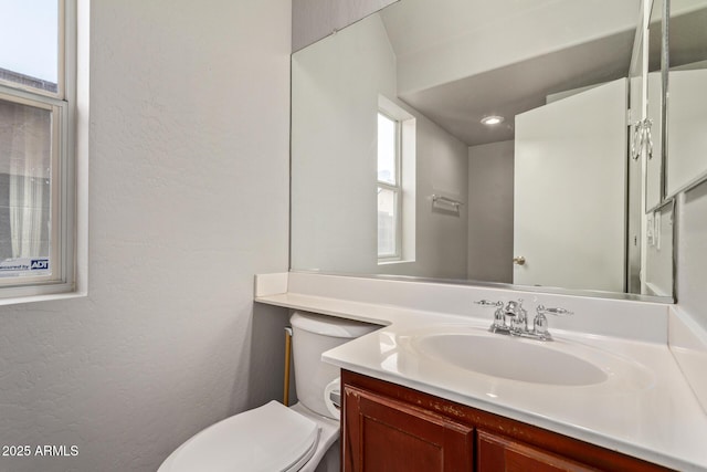 half bathroom with toilet, a textured wall, and vanity