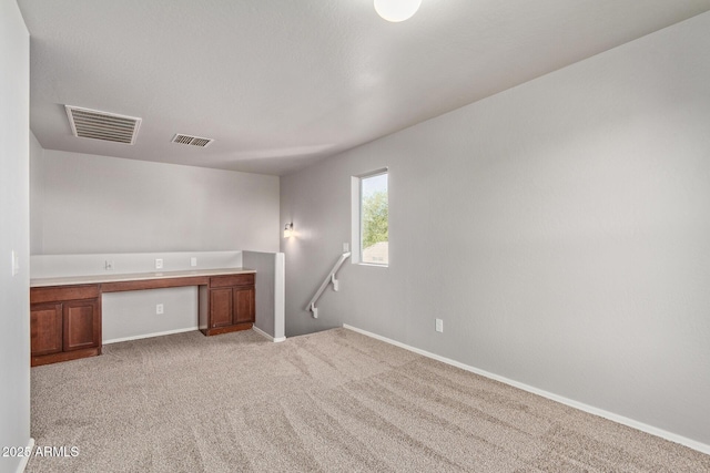 unfurnished room with baseboards, visible vents, light carpet, and built in study area