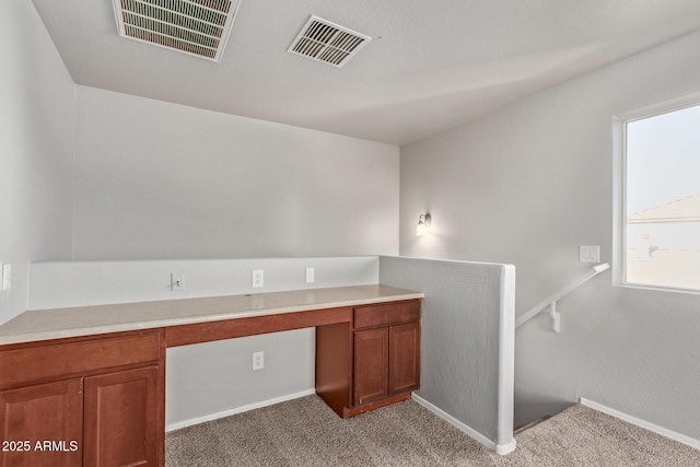 unfurnished office featuring visible vents, built in desk, and light carpet