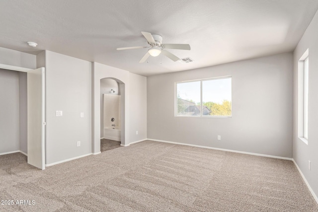 unfurnished bedroom featuring connected bathroom, arched walkways, visible vents, and carpet floors