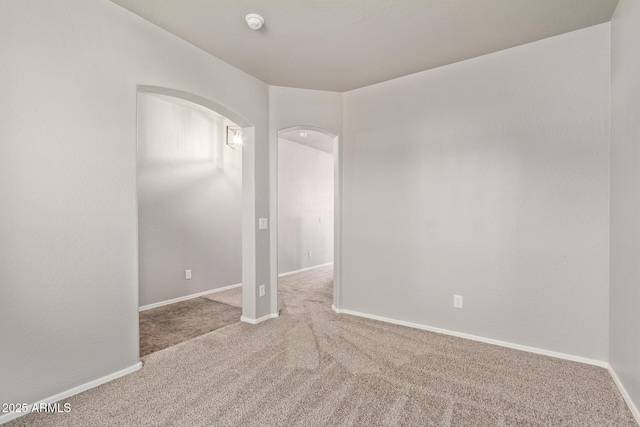 carpeted spare room featuring arched walkways and baseboards