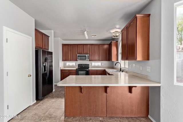 kitchen featuring black appliances, a peninsula, light countertops, and plenty of natural light
