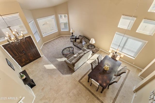 carpeted living area featuring a towering ceiling, an inviting chandelier, and baseboards