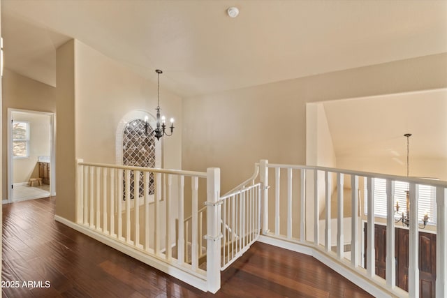 hallway with baseboards, lofted ceiling, hardwood / wood-style floors, an upstairs landing, and a notable chandelier