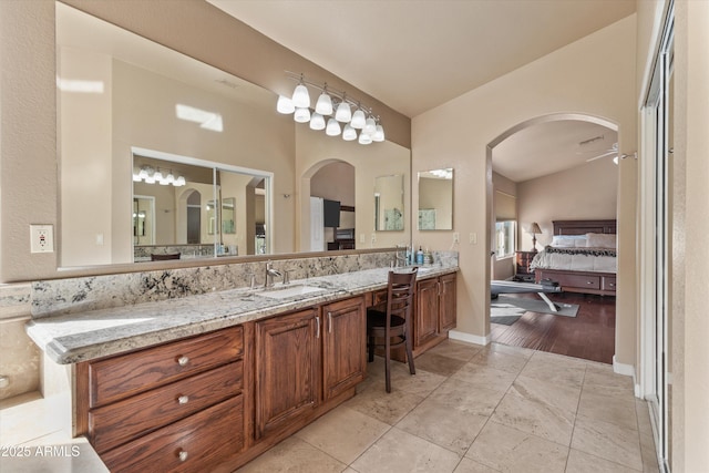 ensuite bathroom with double vanity, vaulted ceiling, a sink, ensuite bath, and tile patterned flooring