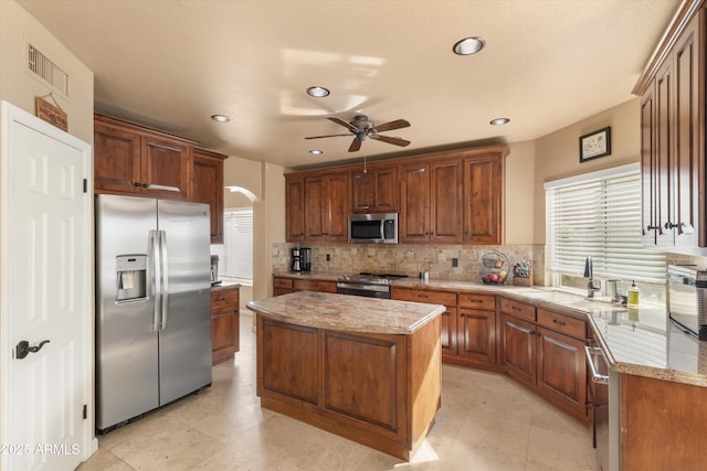 kitchen with a sink, visible vents, appliances with stainless steel finishes, backsplash, and a center island