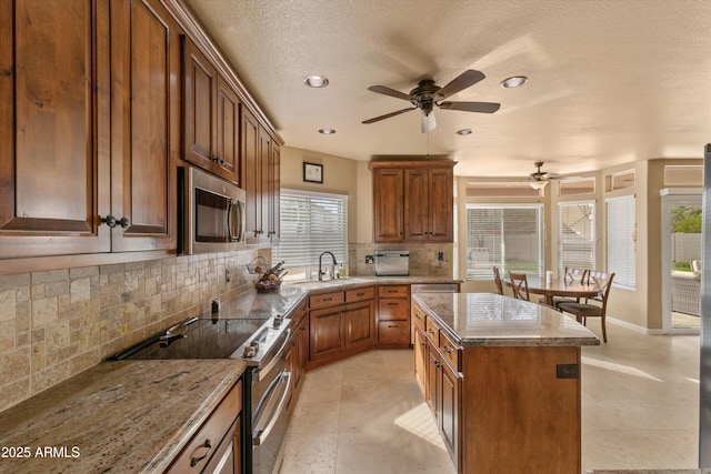 kitchen featuring a sink, a center island, appliances with stainless steel finishes, backsplash, and brown cabinets