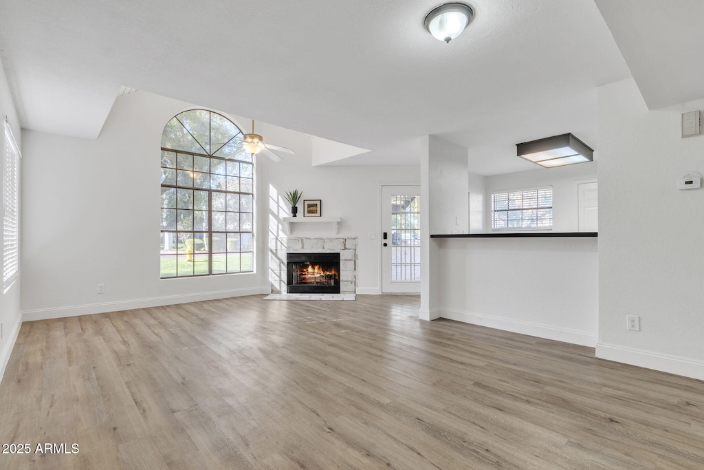 unfurnished living room featuring ceiling fan, a stone fireplace, and light hardwood / wood-style floors