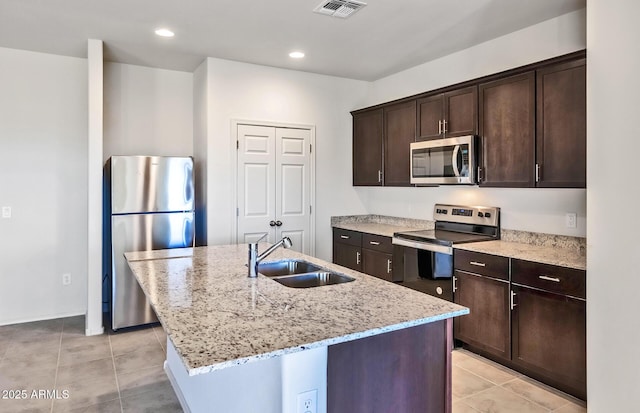 kitchen featuring a kitchen island with sink, sink, light stone counters, and stainless steel appliances