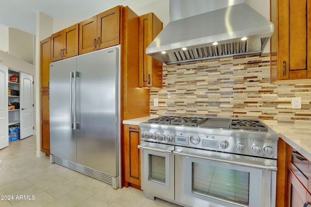 kitchen with wall chimney exhaust hood, high quality appliances, light stone counters, and backsplash