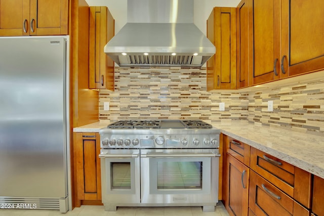 kitchen featuring decorative backsplash, light stone countertops, wall chimney range hood, light tile patterned floors, and high quality appliances