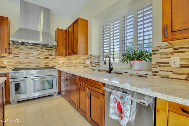 kitchen featuring backsplash, light stone counters, wall chimney exhaust hood, stainless steel appliances, and sink