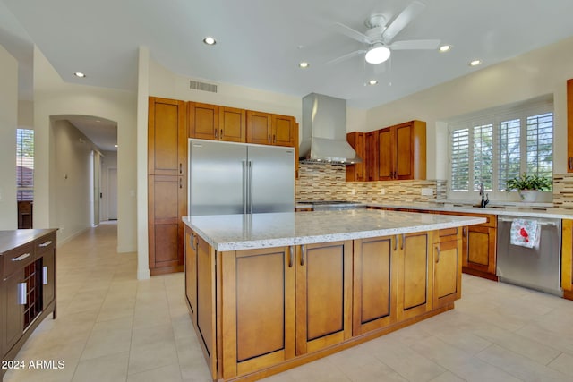 kitchen with a center island, sink, stainless steel appliances, wall chimney range hood, and light stone counters