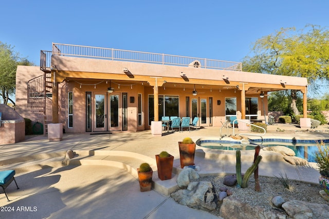 rear view of property featuring french doors, ceiling fan, a swimming pool with hot tub, a balcony, and a patio area