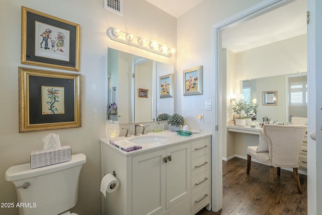 bathroom with vanity, wood finished floors, visible vents, baseboards, and toilet