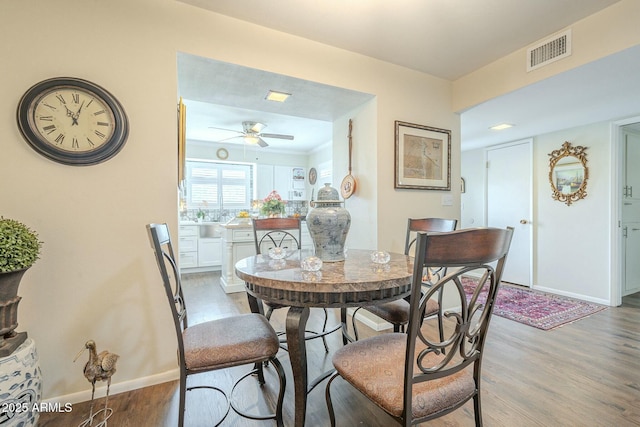 dining space with visible vents, baseboards, wood finished floors, and a ceiling fan