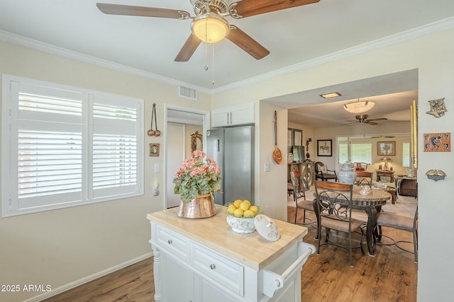 kitchen with wood finished floors, visible vents, white cabinets, crown molding, and stainless steel fridge