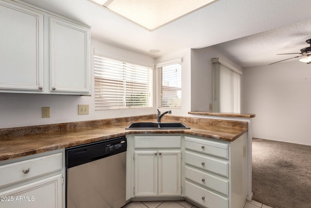 kitchen with dark countertops, ceiling fan, light colored carpet, stainless steel dishwasher, and a sink