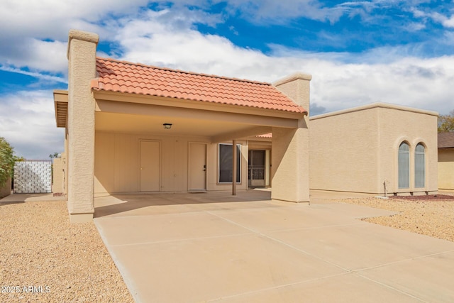 rear view of house featuring stucco siding, driveway, a tile roof, and a patio