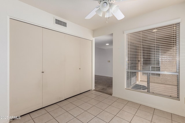 unfurnished bedroom with visible vents, light carpet, a closet, light tile patterned floors, and ceiling fan