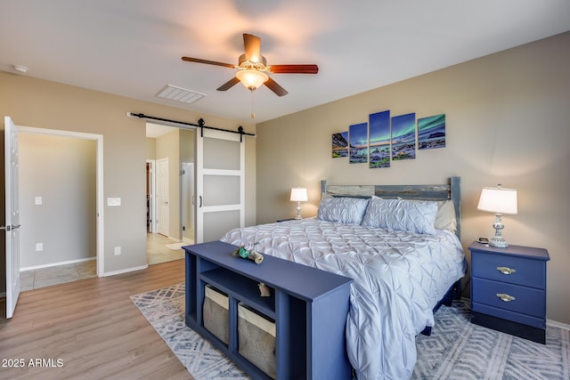 bedroom featuring a barn door, ceiling fan, and light wood-type flooring