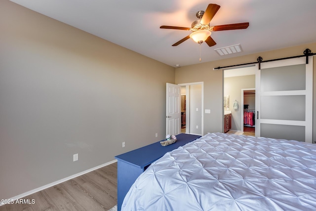 bedroom with a walk in closet, a barn door, ceiling fan, and light hardwood / wood-style flooring