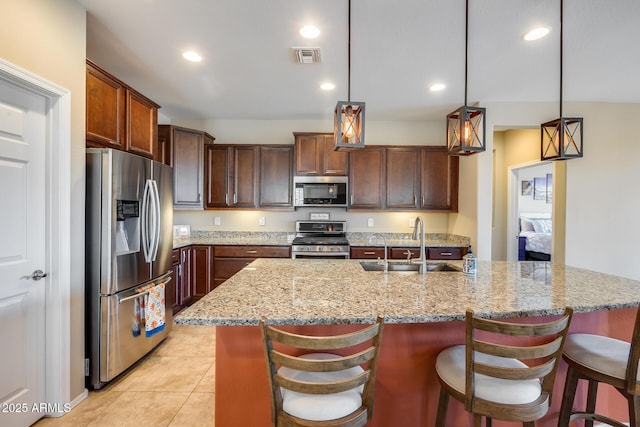 kitchen featuring sink, light stone counters, hanging light fixtures, stainless steel appliances, and a kitchen island with sink