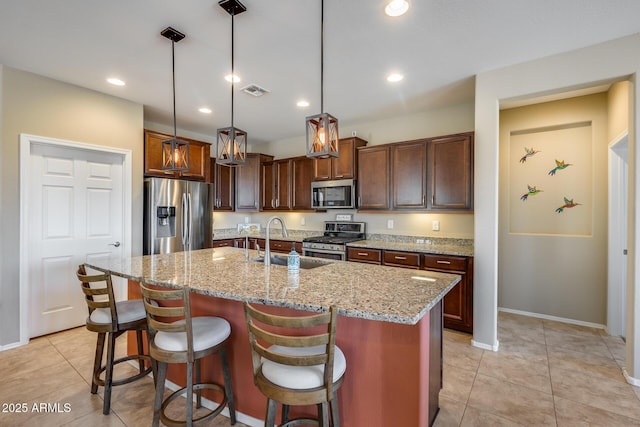 kitchen with appliances with stainless steel finishes, sink, pendant lighting, and a kitchen island with sink