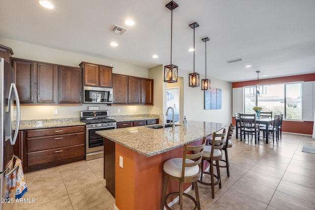 kitchen featuring sink, light stone counters, hanging light fixtures, an island with sink, and stainless steel appliances