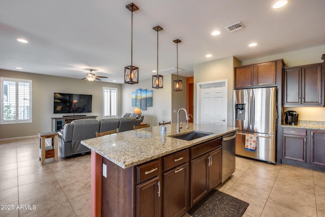 kitchen featuring an island with sink, sink, hanging light fixtures, stainless steel appliances, and light stone countertops