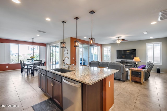 kitchen featuring pendant lighting, dishwasher, sink, light stone counters, and a center island with sink