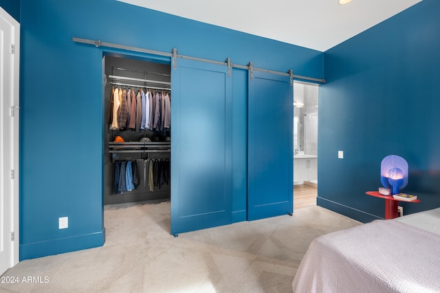 carpeted bedroom with a barn door, a closet, and ensuite bath