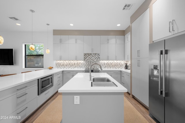 kitchen featuring sink, stainless steel appliances, an island with sink, decorative light fixtures, and white cabinets