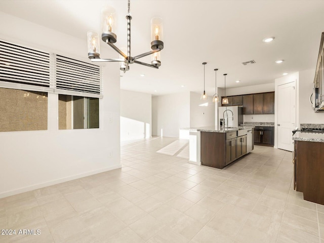 kitchen featuring pendant lighting, sink, dark brown cabinetry, light stone countertops, and a center island with sink