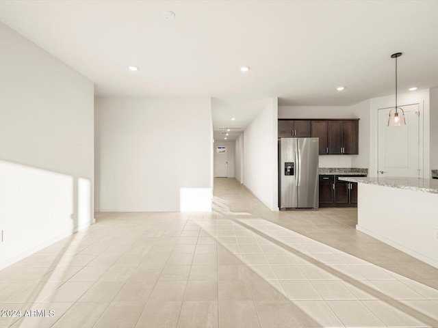 interior space featuring stainless steel refrigerator with ice dispenser, hanging light fixtures, dark brown cabinets, light tile patterned floors, and light stone countertops