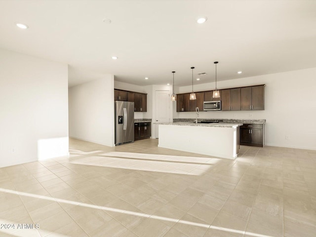 kitchen featuring pendant lighting, sink, stainless steel appliances, light stone counters, and a center island with sink