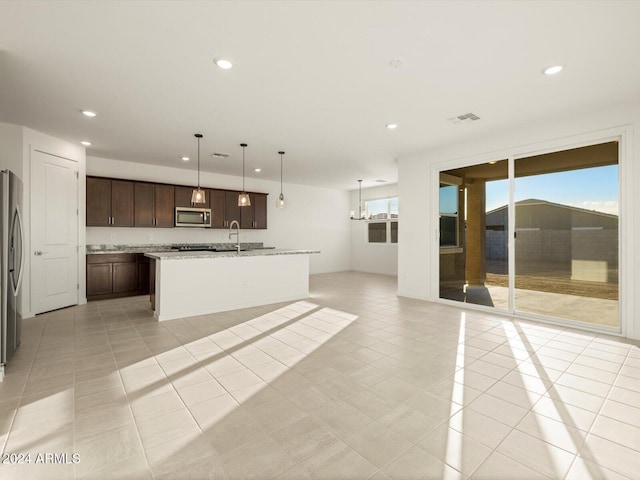 kitchen featuring hanging light fixtures, stainless steel appliances, dark brown cabinetry, light stone countertops, and light tile patterned flooring