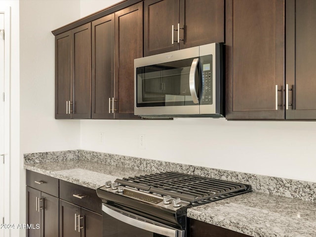 kitchen featuring stainless steel appliances, light stone counters, and dark brown cabinetry