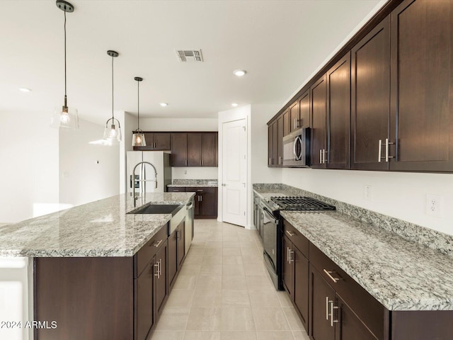 kitchen with light stone counters, decorative light fixtures, a center island with sink, and appliances with stainless steel finishes