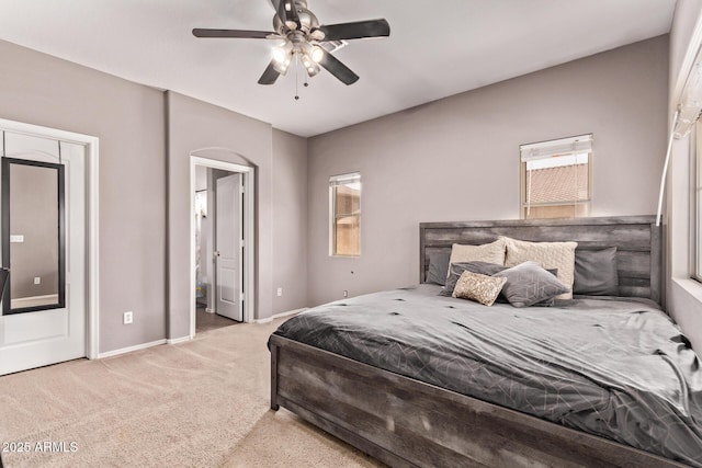 carpeted bedroom featuring arched walkways, baseboards, ensuite bathroom, and ceiling fan