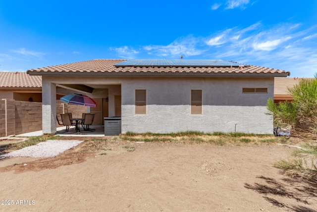 back of house featuring fence, stucco siding, roof mounted solar panels, a patio, and a tiled roof