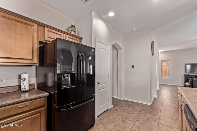 kitchen featuring light tile patterned floors, baseboards, stainless steel dishwasher, and black fridge