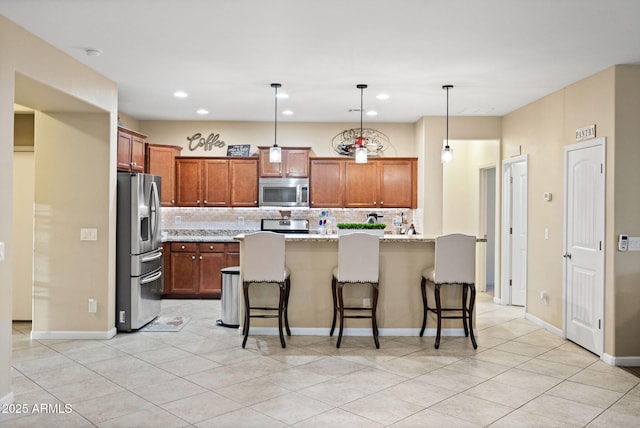 kitchen with light stone counters, appliances with stainless steel finishes, a kitchen breakfast bar, decorative light fixtures, and backsplash